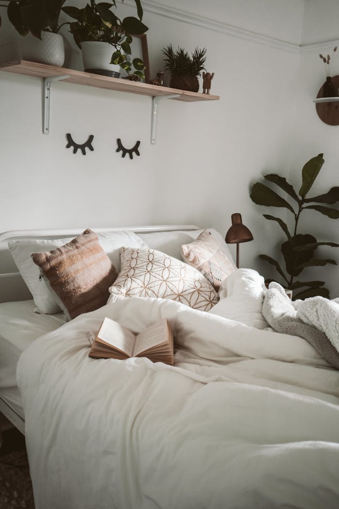 Warm and inviting bedroom setup with decorative pillows, plants, and an open book for a cozy ambiance.